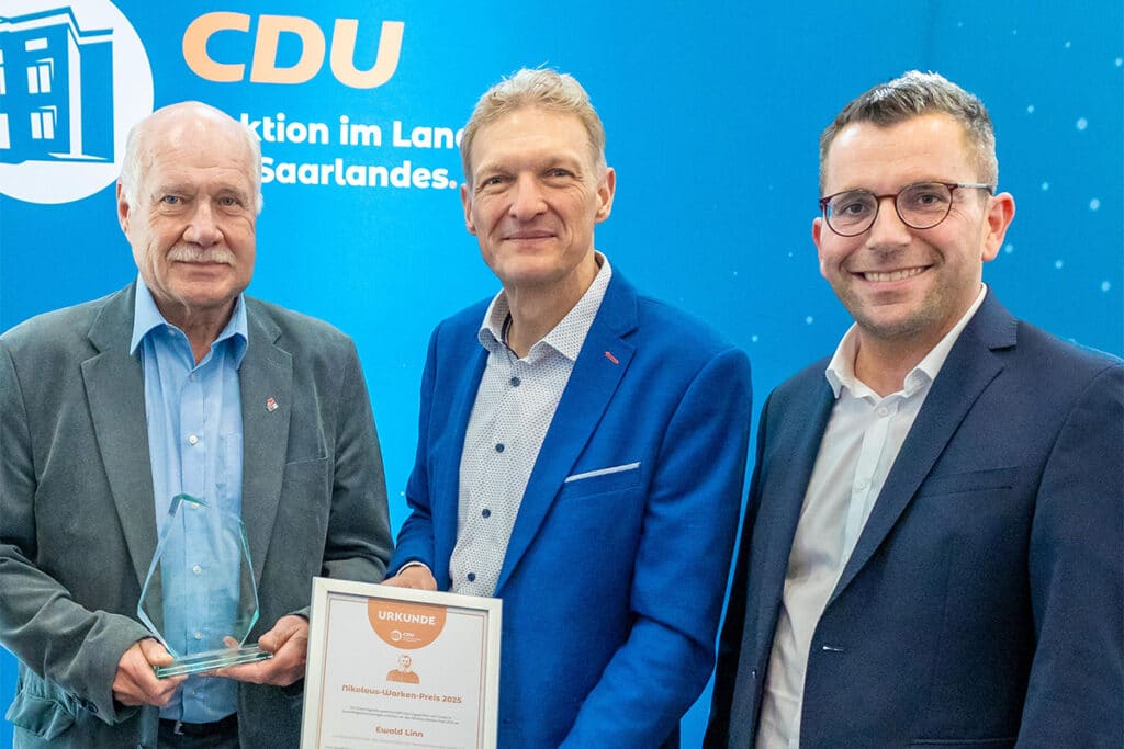 Drei Personen halten eine Urkunde und posieren für ein Foto.